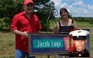 The parents of Marine Lance Cpl. Jacob Lugo hold a street sign on a road being dedicated in their son's honor. Lugo was killed in action in 2004 (Photo Credit: Bill Castleman; Military Times).