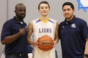 Coram Deo Academy Boys Basketball Head Coach Email Asante (left) and Assistant Coach Fonzo Martinez present Logan McClure with the game ball after he broke 1,000 points in a season.