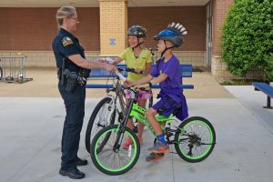 A Flower Mound police officer "tickets" kids with a 7-Eleven Operation Chill coupon for being safe by wearing helmets while riding their bikes.