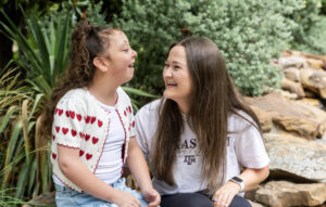 A young girl and a young woman both laugh in an outdoor setting.